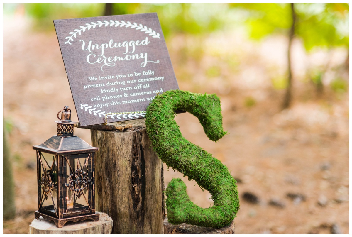 Whimsical Woodland Fall Wedding at mountain memories at thorpewood in thurmont maryland in october by sarah & dave photography richmond wedding photographer wooden forest inspired welcome sign with white letters greenery ferns and log easel outdoor ceremony in the woods moss covered letter unplugged ceremony sign lantern tree stump forest woodland inspired ceremony decorations decor