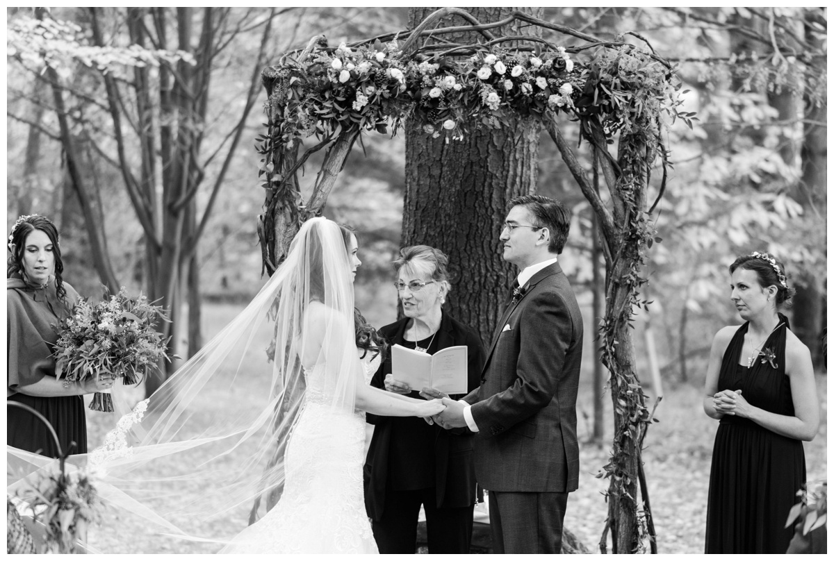 Whimsical Woodland Fall Wedding at mountain memories at thorpewood in thurmont maryland in october by sarah & dave photography richmond wedding photographer forest inspired outdoor ceremony in the woods bride and groom at altar floral and stick woodland inspired wedding floral arch backdrop centerpiece black and white photo