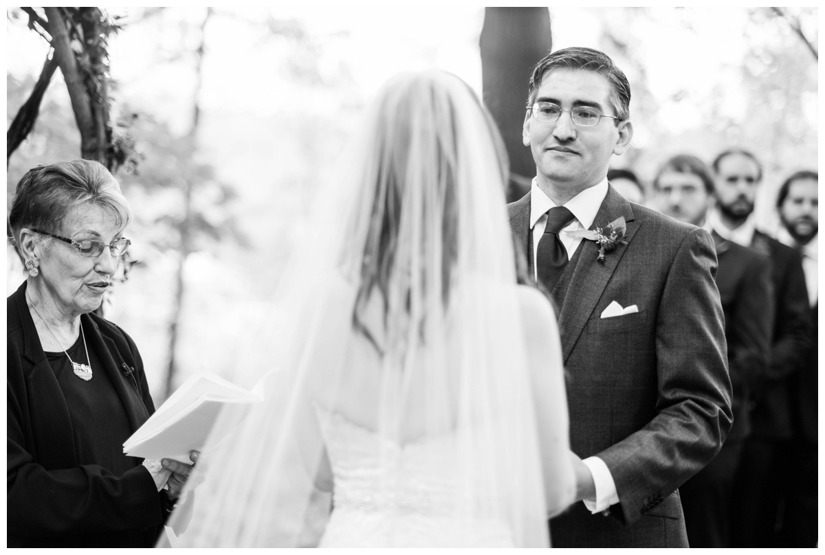 Whimsical Woodland Fall Wedding at mountain memories at thorpewood in thurmont maryland in october by sarah & dave photography richmond wedding photographer forest inspired outdoor ceremony in the woods bride and groom at altar groom in focus holding hands black and white photo