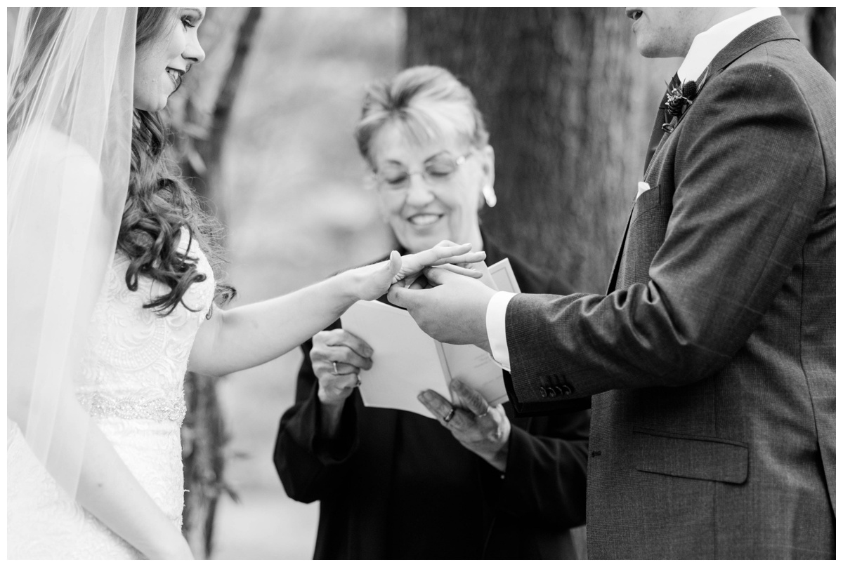 Whimsical Woodland Fall Wedding at mountain memories at thorpewood in thurmont maryland in october by sarah & dave photography richmond wedding photographer forest inspired outdoor ceremony in the woods bride and groom at altar groom placing ring on brides finger black and white photo