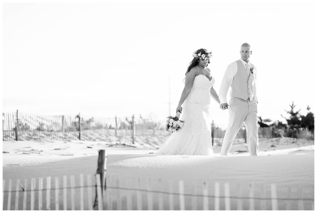 black and white photo of bride and groom walking on sand at sunset bride is wearing allure bridals wedding dress by maryland bridal boutique k & b bridals and groom is wearing mens wearhouse suit by richmond wedding photographer Sarah & Dave Photography
