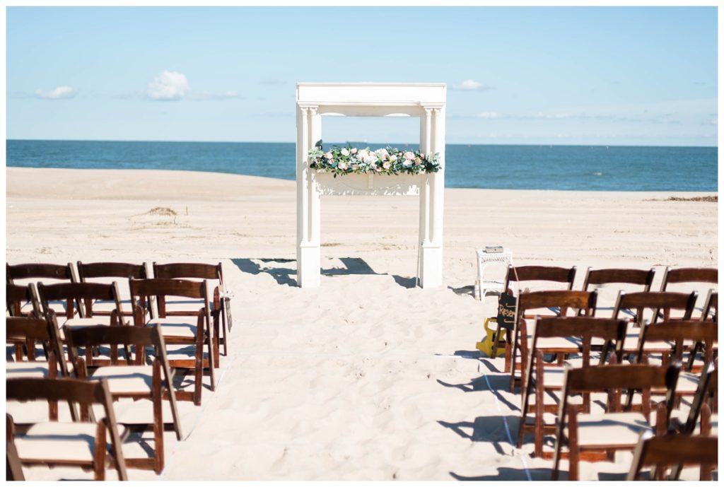 romantic summer wedding at the beach with white ceremony arch, flower garland, sand, folding chairs, and ocean views