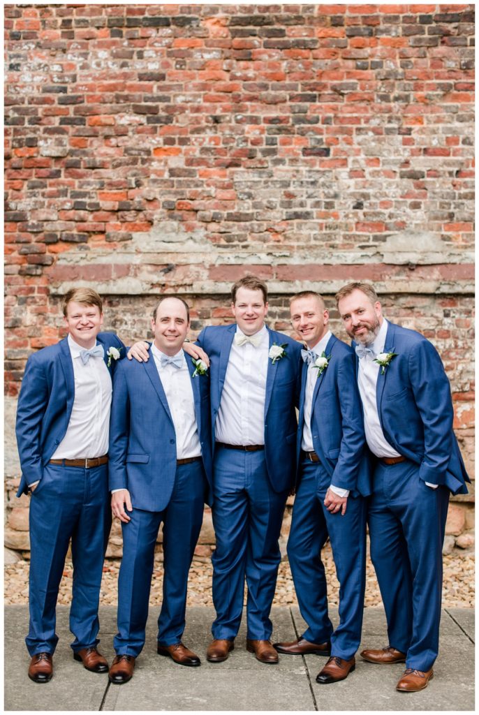 charming summer wedding at historic tredegar ironworks and civil war museum - photo of wedding party - groom and groomsmen in front of brick wall wearing indigo suits, brown leather shoes, and pale yellow and light blue and white striped bowties by richmond rva and central virginia wedding photographer, sarah & dave photography
