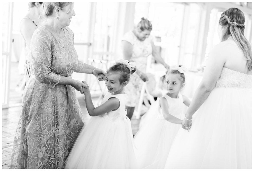 black and white wedding reception photo at the boathouse at sunday park wedding venue in richmond virginia in the summer - flower girls dancing with bride holding hands - happy - joy filled - by rva wedding photographer sarah & dave photography