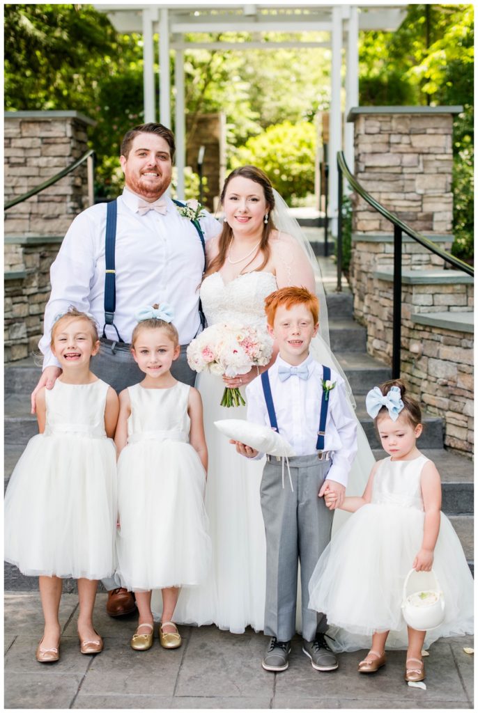 flower girls with white dresses, gold slipper shoes, light blue bows, ringbearer and groom wearing navy blue suspenders and light grey suit pants - red hair - at richmond wedding venue - outdoors - at the boathouse weddings - the boathouse at sunday park - wedding party photo - by richmond rva wedding photographer, sarah & dave photography