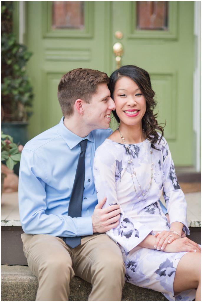 couple smiling - sitting next to each other - in front of green door - on porch home - wooden - brass - purple dress - blue button up shirt and tie - dressy engagement photo ideas and inspiration outdoors in richmond virginia rva