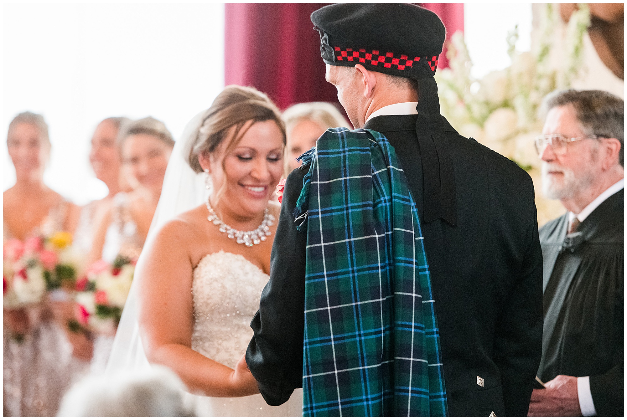 ceremony photo. bride and groom holding hands. groom is wearing kilt and tartan. bride is wearing princess cut ballgown wedding dress that is sparkly. dover hall estate ballroom venue is in the backdrop. 
