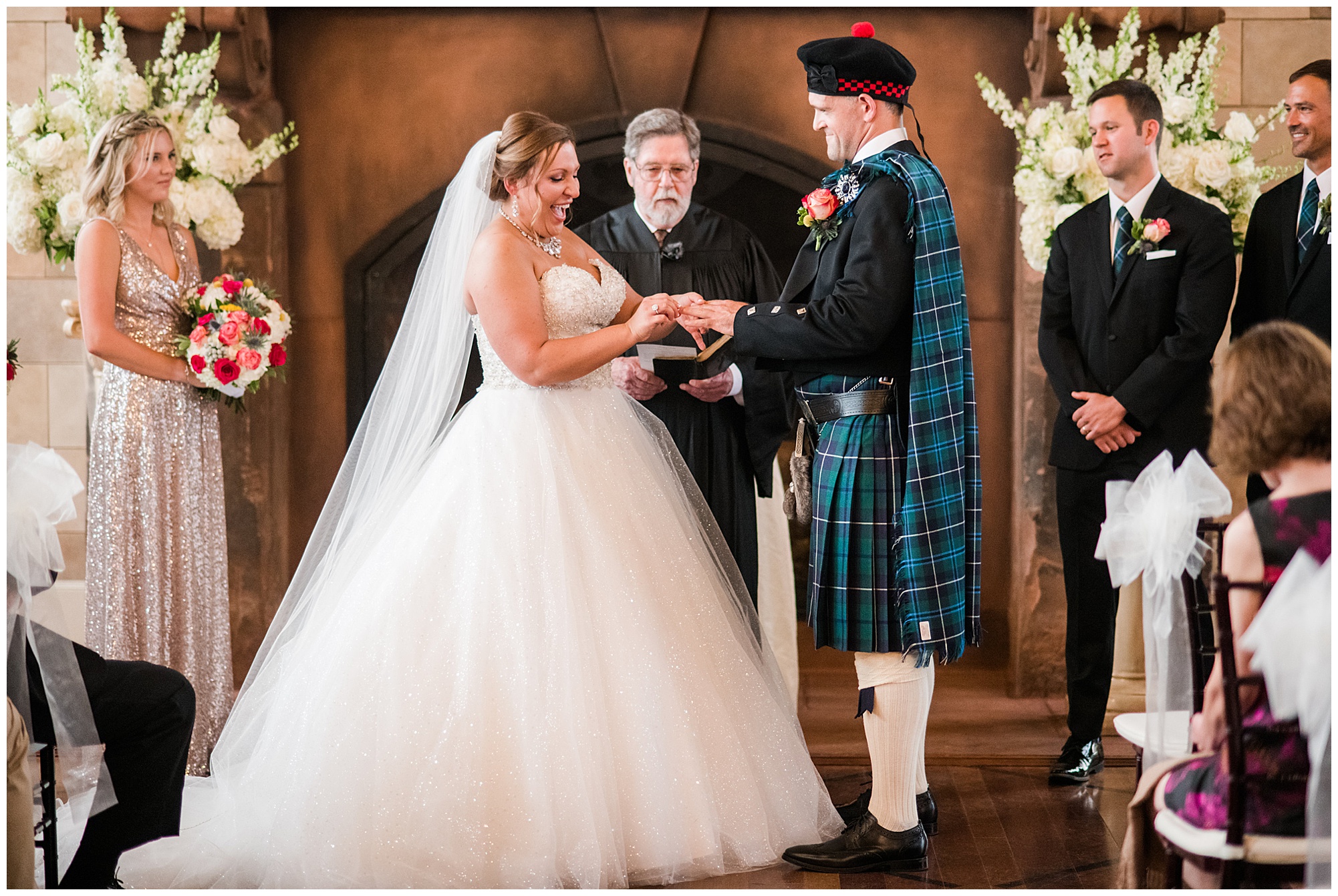 ceremony photo. bride and groom holding hands. groom is wearing kilt and tartan. bride is wearing princess cut ballgown wedding dress that is sparkly. dover hall estate ballroom venue is in the backdrop. 